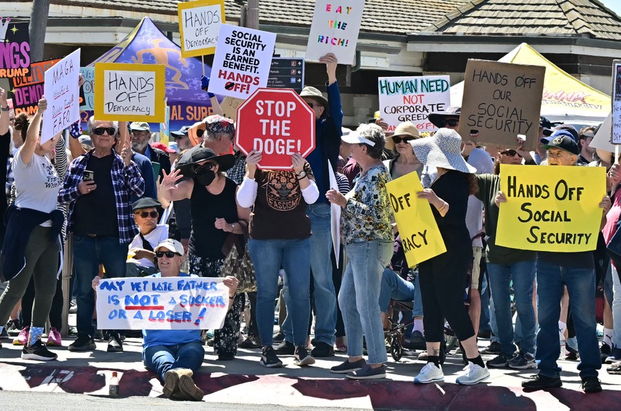 A group of demonstrators holds protest signs, including one that reads "Stop the DOGE!"