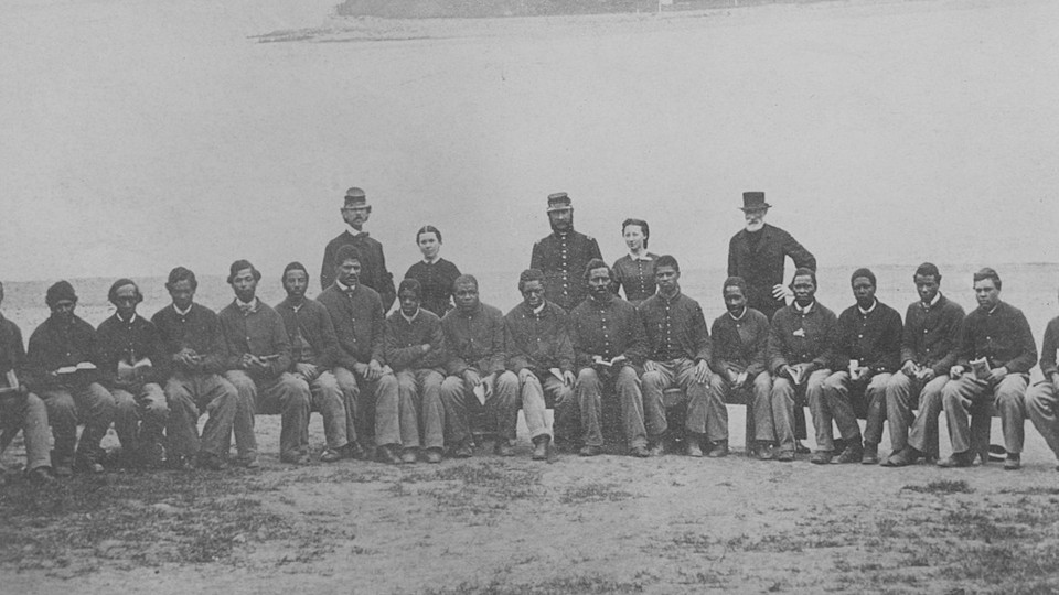 Black Civil War soldiers sitting in a row in front of standing white officers