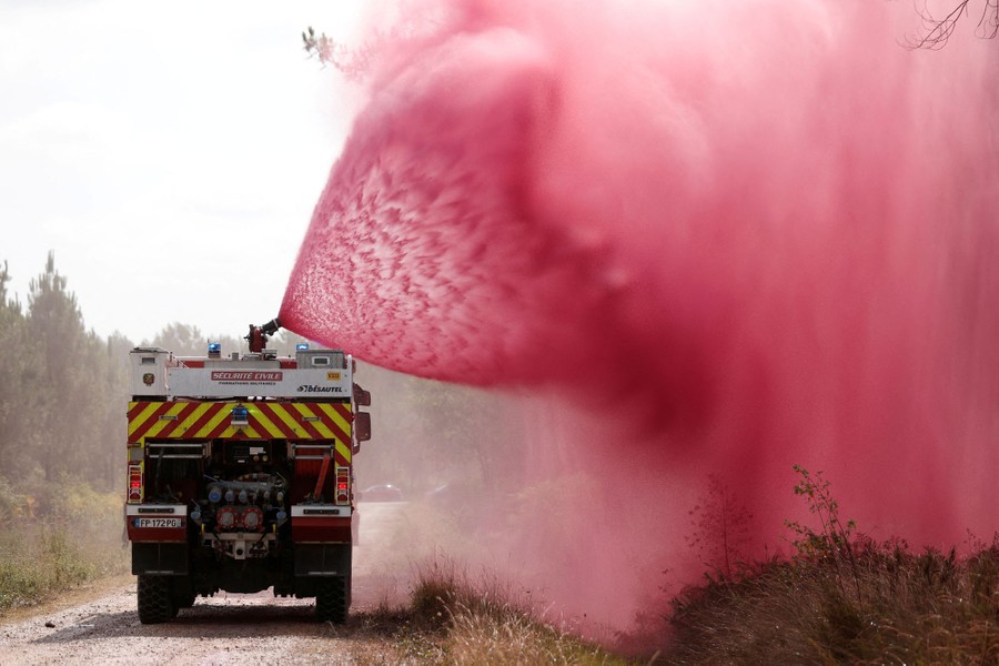 A fire truck sprays red fire retardant in a broad cone toward a wildfire.