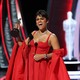Ariana DeBose in a red dress holds an Oscar statue aloft.