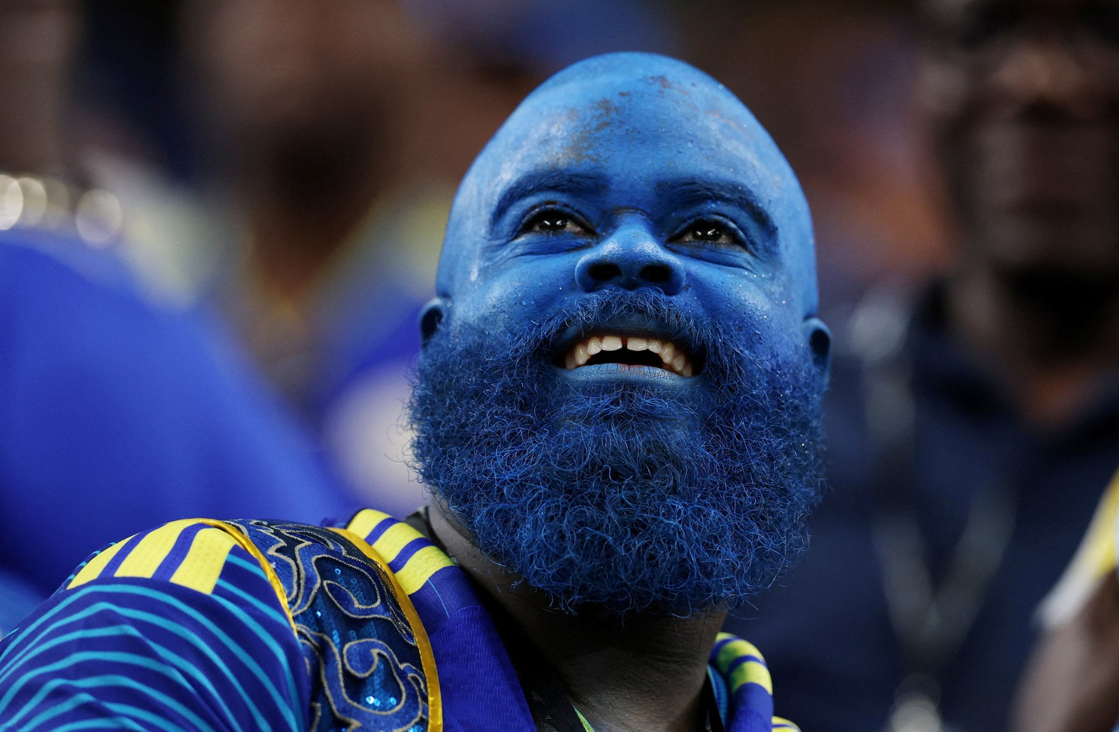 A soccer fan, their entire head, face, and beard covered in blue makeup