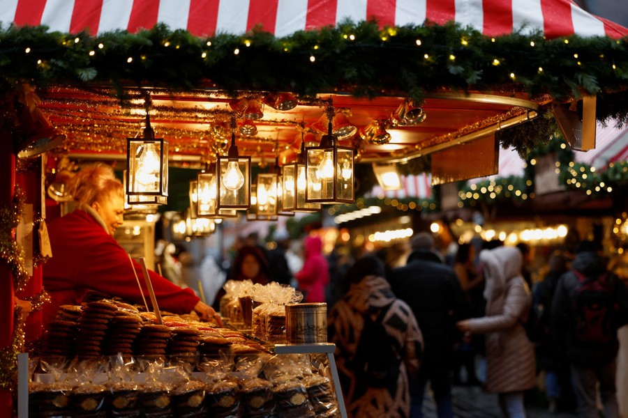 A person works in a festive market stall as people walk by.