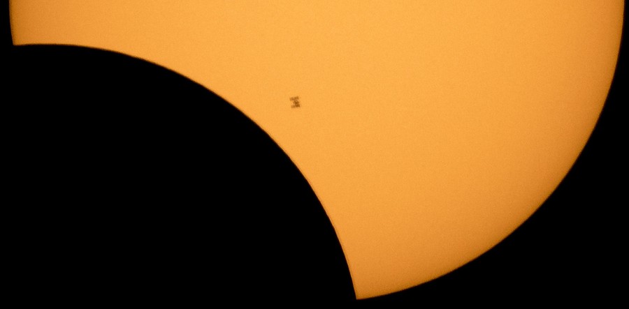 The tiny outline of the International Space Station is seen in silhouette in front of a partly-eclipsed sun.