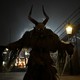 A person wearing a frightening demon mask and costume, dressed as Krampus, seen at night, silhouetted by a light