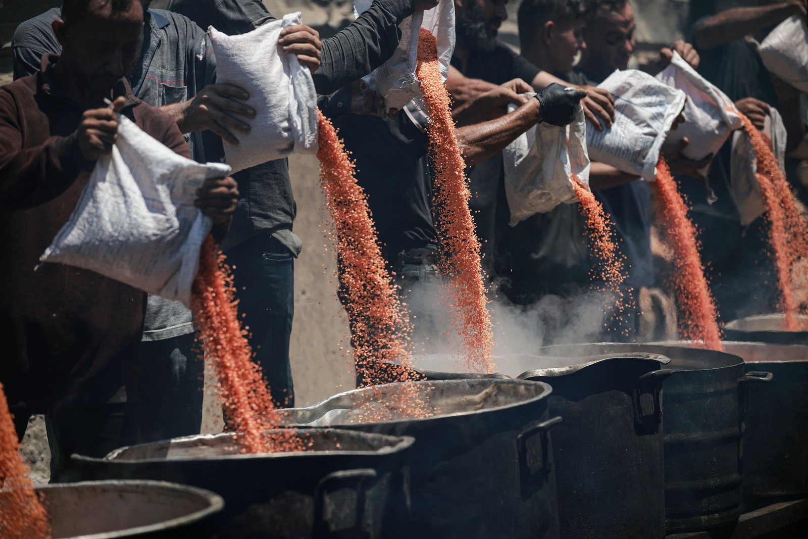 Seven or eight people pour sacks of lentils into large cooking pots.