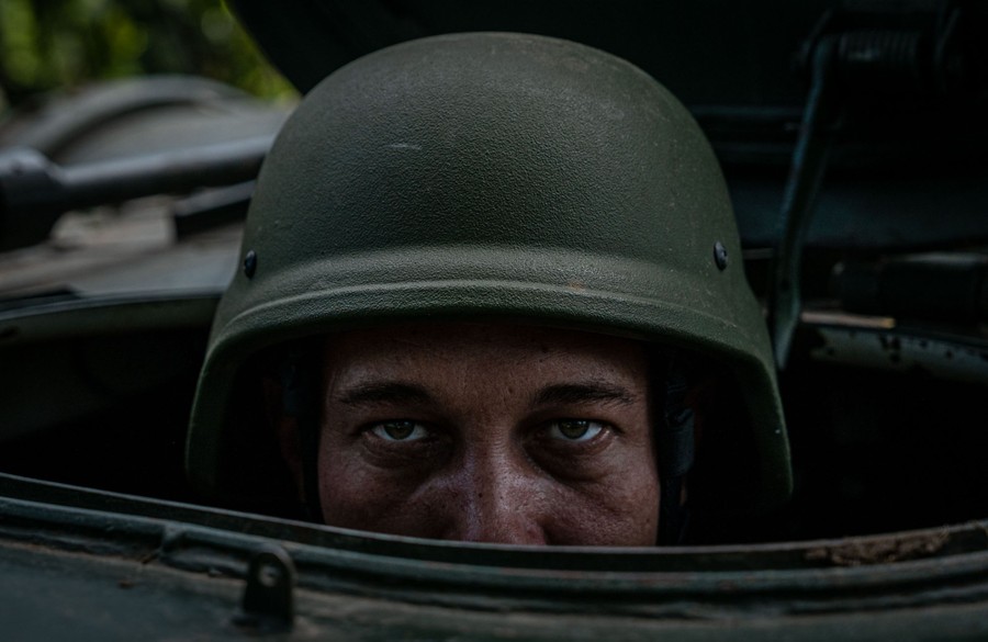 A close view of a soldier wearing a helmet, sitting inside mobile artillery vehicle.