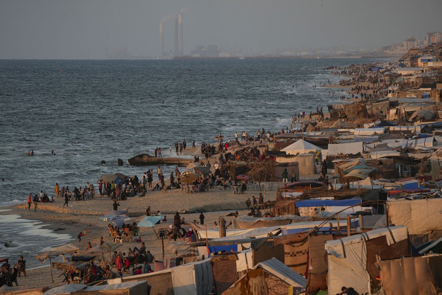Many tents and people line the shore on a beach.