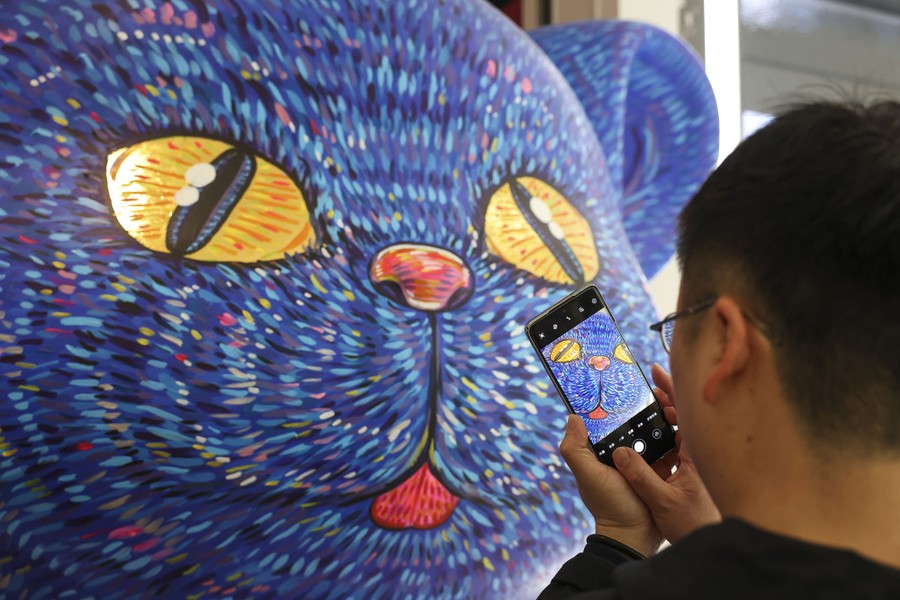 A person uses a phone to take a photo of a large cat-shaped sculpture.