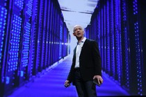 Jeff Bezos stands in front of a purple, blue, and black data center.