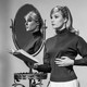 A woman stands next to a mirror reflecting her image
