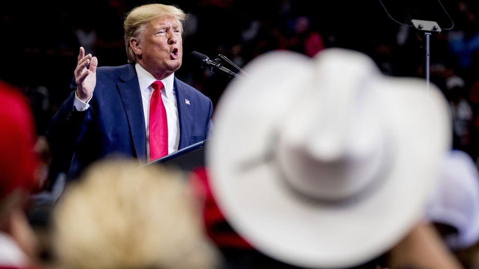 President Trump speaks into a microphone at a campaign rally as supporters, one wearing a white cowboy hat, look on.