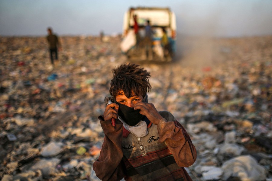 A young person poses for a picture, standing in a broad landfill.