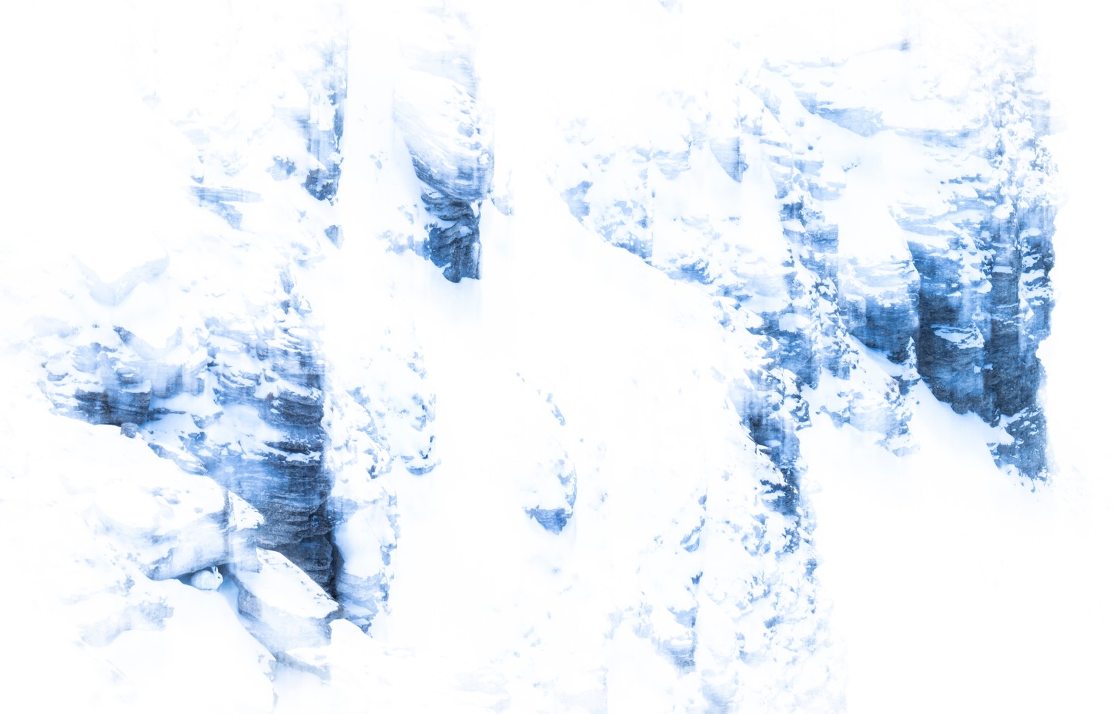 A small white hare sits in the entrance to a cave, surrounded by a snow-covered rocky mountainside.