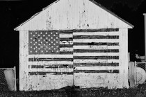 Black-and-white photo of a wooden house with the American flag painted on it