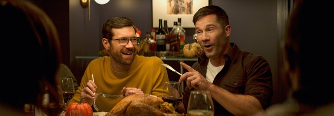 Billy Eichner and Luke Macfarlane laughing at a dinner table in "Bros"