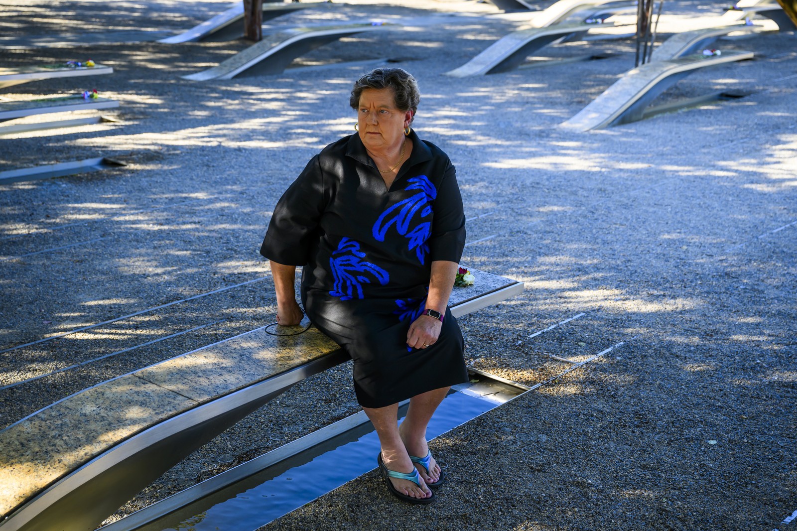 A person rests on a memorial bench, looking off camera.