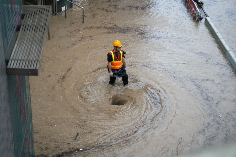 A worker stands in knee-deep water, beside a small whirlpool, as floodwater is drained from a road.