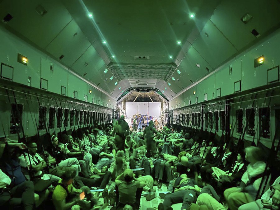 A view of the interior of a military aircraft with dozens of people seated on the floor.