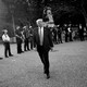 Donald Trump, with police officers behind him, walks outside the White House. The photo is black and white.