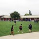 Students walk across a grassy field in front of a school building. 