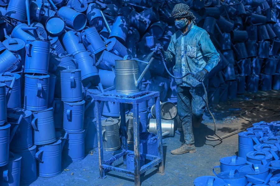 A worker paints a large stack of watering cans.