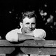 Black-and-white photo of Edmund White smiling, in a white shirt