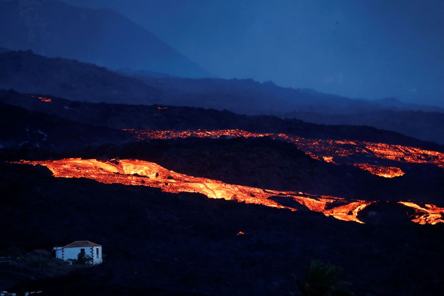 Lava flows past a house at night.