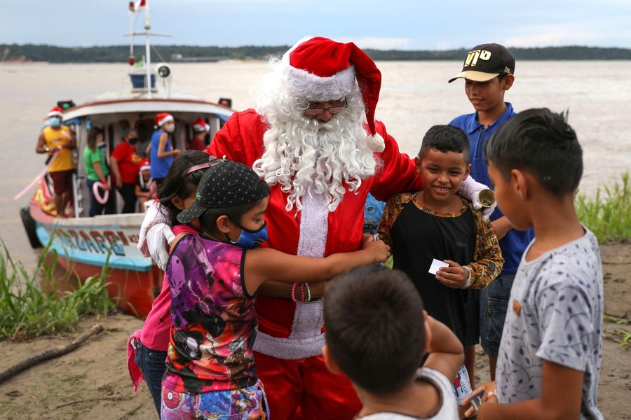 A man dressed as Santa Claus embraces several children on a riverbank.