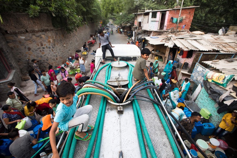 People use hoses to collect drinking water from a tanker truck.