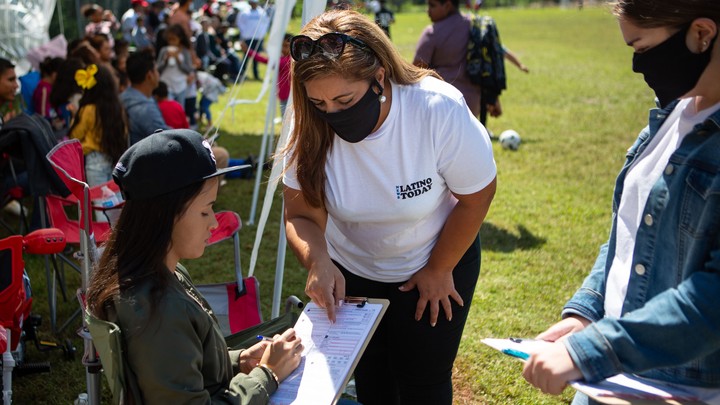 Two female political organizers speak to another woman on the sidelines of a soccer match.