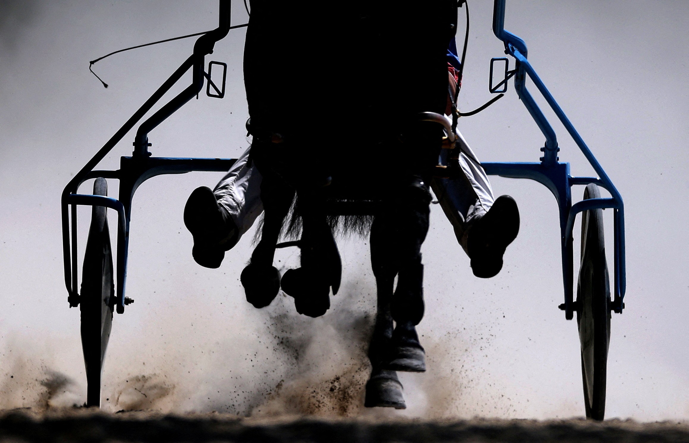 A close view of a horse's hooves and outline of a carriage during a harness race.
