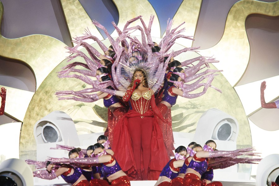 Beyoncé performs onstage with a group of dancers forming a design with many outstretched arms.