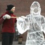 A woman raises an ice-scraping tool next to an ice sculpture of Jesus Christ.