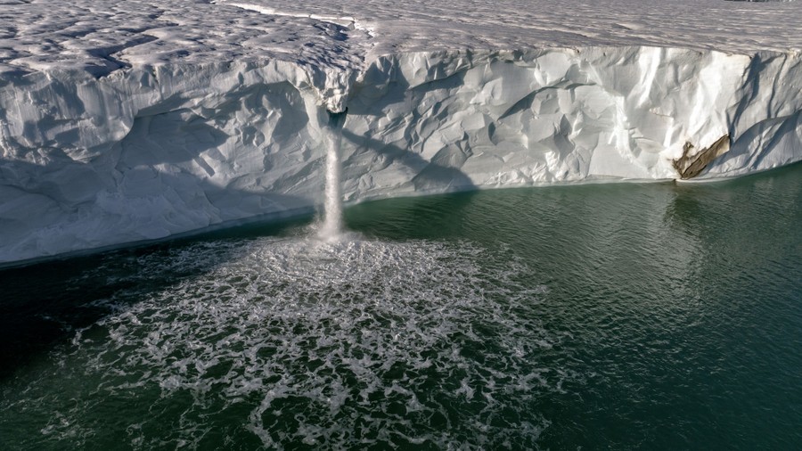 Water flows off the edge of a glacier, splashing into the sea.
