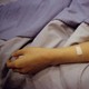 A patient's arm lies flopped on a bed, a bandage on the forearm
