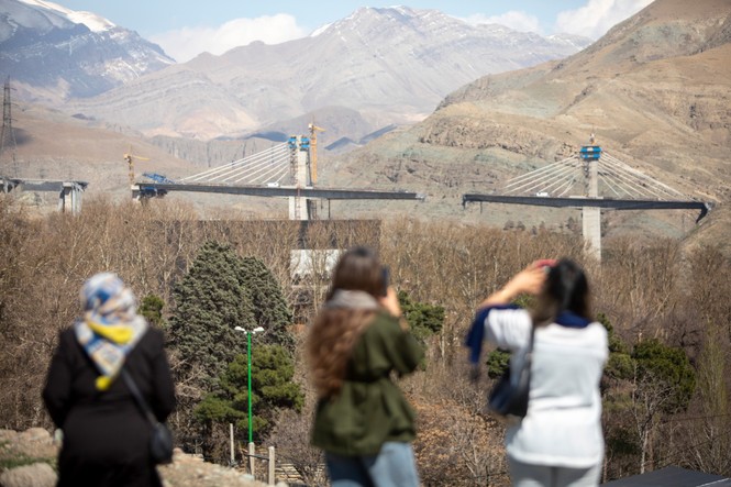 Three women taking photos and looking at a destroyed bridge in the distance.