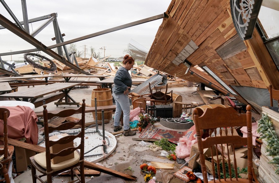 A person stands amid debris of a building destroyed by a tornado.