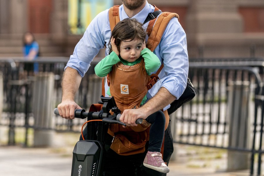 A child sits in strap-on baby carrier covering their ears.
