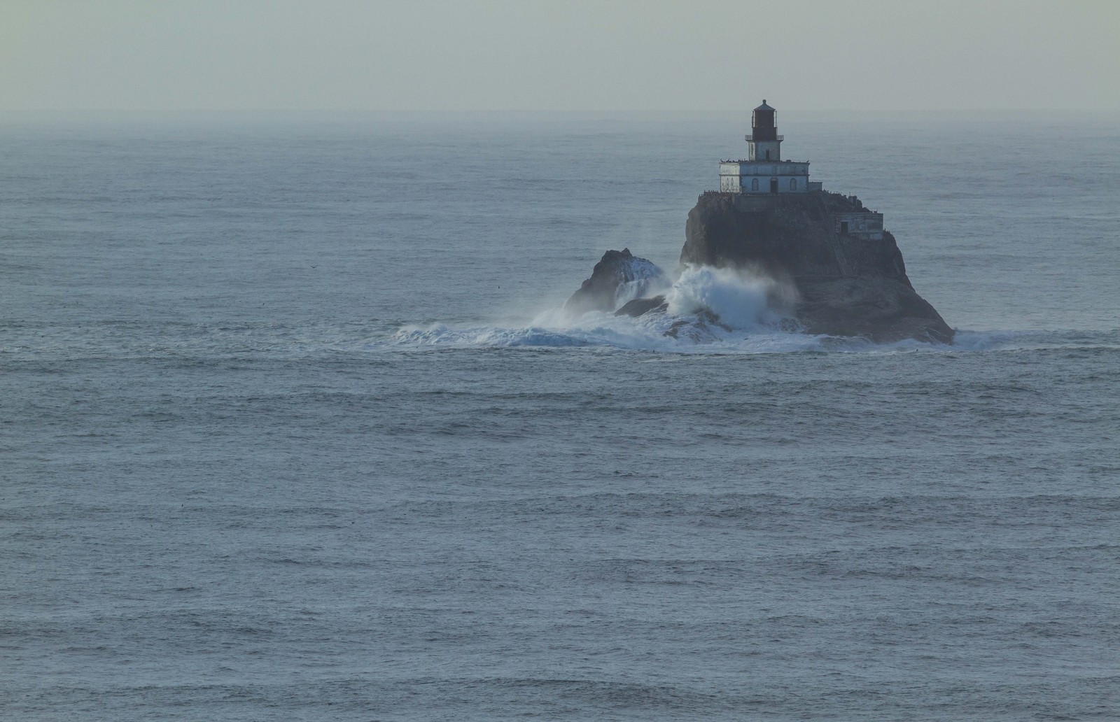 A deactivated lighthouse sits on a small rock outcrop in the ocean.