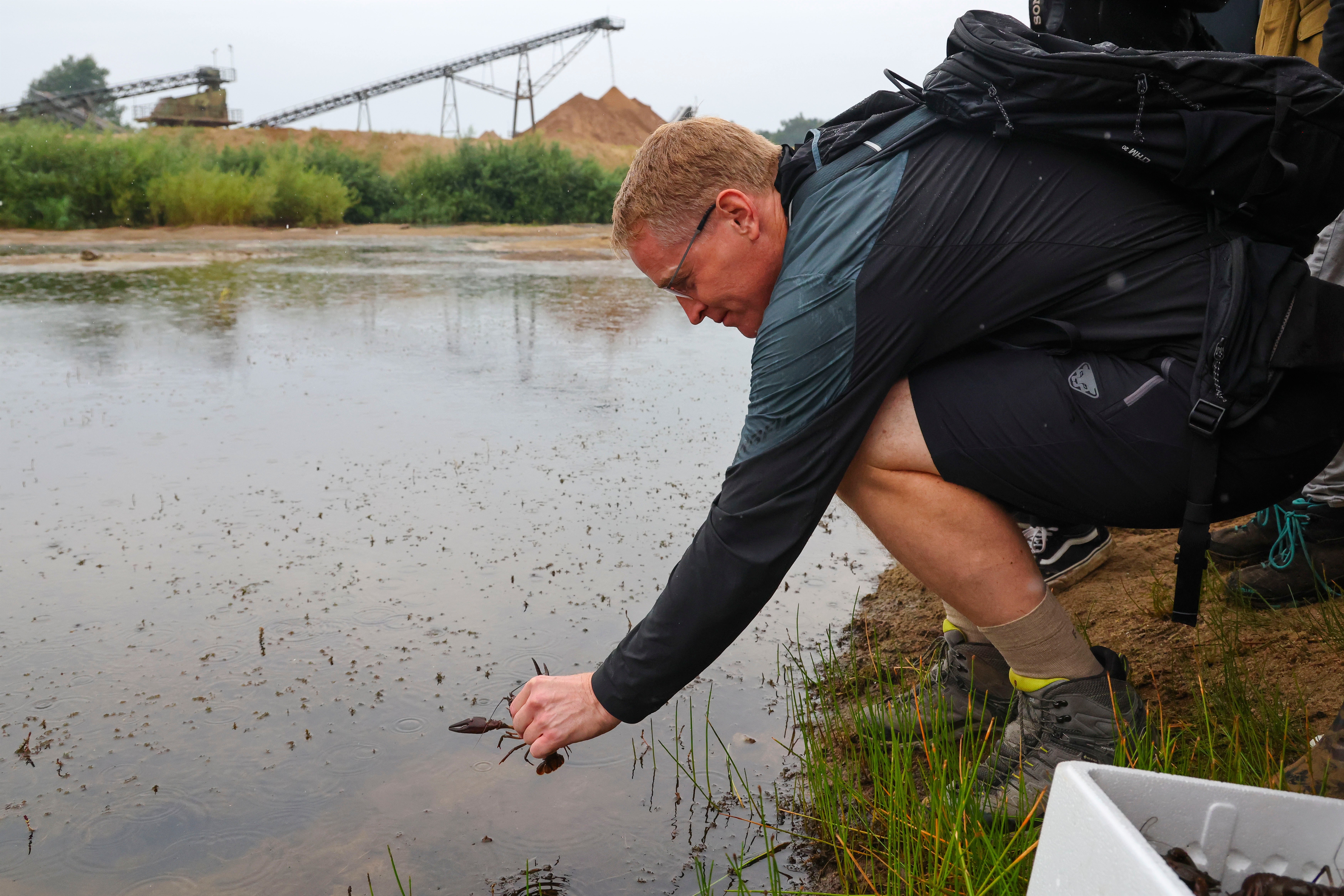 A person kneels down to release a crayfish into a pond.