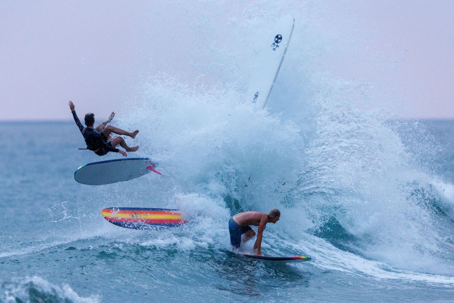 Several surfers are seen in various positions above a crashing wave.