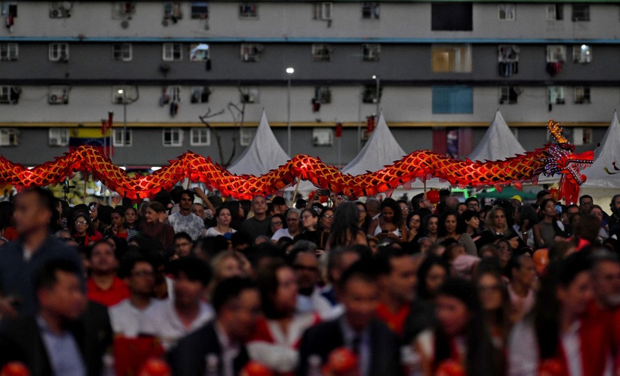 A crowd watches a performance as dancers behind them carry a long dragon puppet.