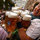 A person smiles while carrying ten large beer mugs in a beer hall.
