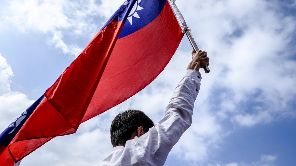 Man holding the Taiwan flag up in the air, in front of a blue sky