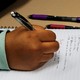 A student holds a pencil above a sheet of notebook paper. The notes appear to be about the government