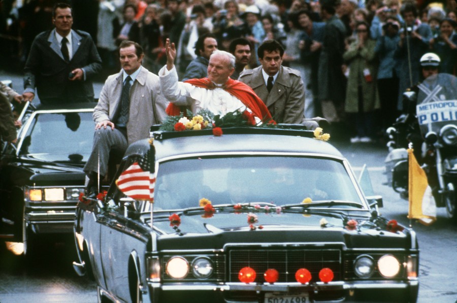 The Pope rides in an open-top car past large crowds.