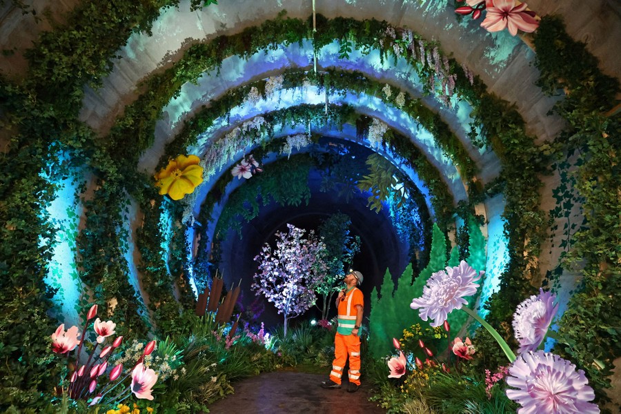 A worker poses inside a large sewer tunnel that has been decorated with many plants.