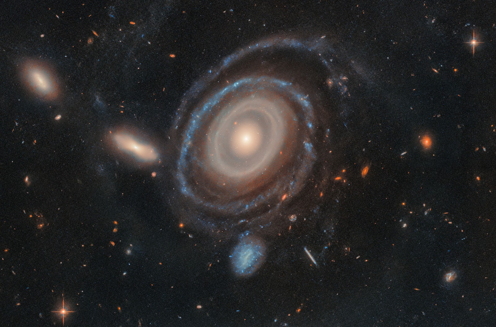 A spiral galaxy displaying by at least nine concentric rings around its core, backdropped by many other smaller, more-distant galaxies