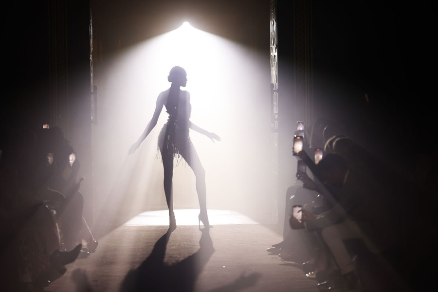 A model walks a runway in front of a bright light.