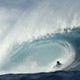 A surfer rides low inside the barrel of a huge breaking wave.